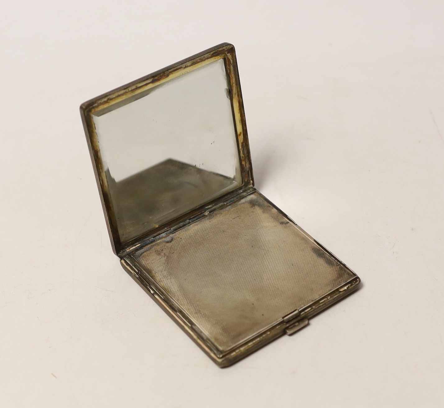An Elizabeth II engine turned silver square compact, with applied yellow metal initials, 'JEM', W.H. Manton Ltd, Birmingham, 1961, 76mm.
